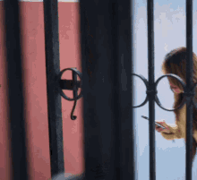 a woman behind a wrought iron fence looks at her phone