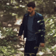 a man in a black jacket is walking through a forest .