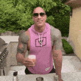 a muscular man in a pink tank top and sunglasses is holding a glass of beer .