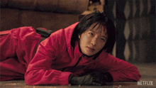 a woman in a red jumpsuit is laying on the floor with a netflix logo behind her