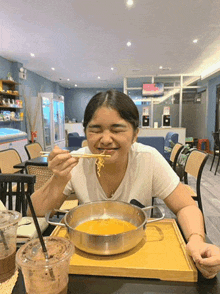 a woman is sitting at a table eating noodles from a pot with chopsticks