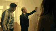 a man in a suit writes on a wall while two other men look on