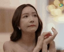a close up of a woman 's face with her hands folded in front of her