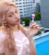 a woman in a pink shirt is holding a pink lollipop in front of a swimming pool .