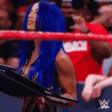 a woman with blue hair is in a wrestling ring holding a microphone .