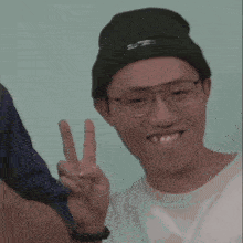 a young man wearing glasses and a beanie is giving a peace sign