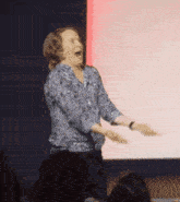 a woman in a blue shirt is standing on a stage with her arms outstretched and a surprised look on her face