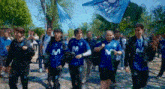 a group of people are walking down a street wearing blue shirts with the letter m on them .
