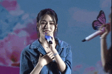 a woman singing into a blue microphone while another woman looks on