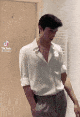 a man wearing a white shirt and grey pants stands in front of a door with a tiktok icon above him