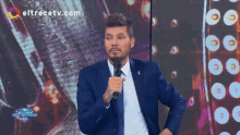 a man in a suit and tie is speaking into a microphone with eltrecetv.com in the background