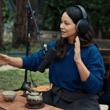 a woman wearing headphones and a blue sweater talks into a microphone