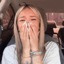 a woman covering her mouth with her hands while sitting in a car