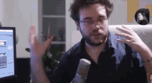 a man with glasses and a beard is talking into a microphone in front of a computer monitor