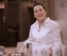 a woman in a white shirt sits on a couch with bottles of perfume in front of her