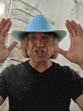 a man wearing a black shirt and a blue cowboy hat making a funny face