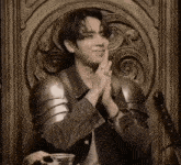a man in armor sits in a chair with his hands together