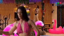 a woman in a pink bikini is dancing next to a pink flamingo float .