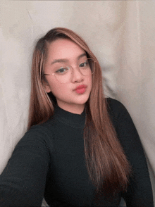 a young woman wearing glasses and a black sweater takes a selfie