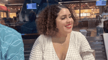 a woman with curly hair is smiling while sitting at a table in a restaurant