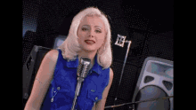 a blonde woman in a blue vest is singing into a microphone in a recording studio .