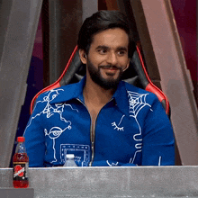 a man in a blue jacket sits at a table with a bottle of dr pepper
