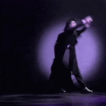 a man in a black coat is dancing on a stage in front of a purple background .