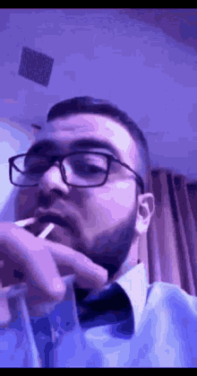 a man wearing glasses and a bow tie is smoking a cigarette in a room .