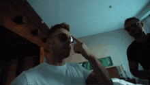 a man adjusts his sunglasses while another man stands behind him