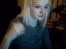 a woman with blonde hair and blue eyes is wearing a black shirt and making a funny face .