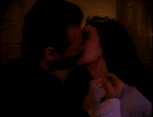 a man and woman are kissing in a dark room with candles in the background