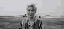 a black and white photo of a man wearing a striped shirt standing in front of an airport .
