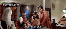 a group of people are standing around a woman who is laying on a bed and asking if her leg is broken .