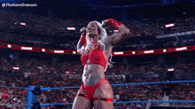 a woman in a red bikini is flexing her muscles in front of a crowd of people .