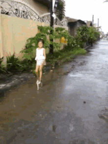 a little girl in a white dress is walking down a rainy street
