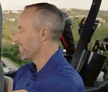 a man in a blue shirt is sitting in a golf cart with golf clubs in it .