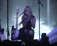 a woman is singing into a microphone while playing a guitar on stage .