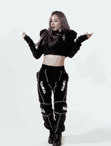 a woman wearing a black crop top and black pants is standing in front of a white background .