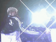 a man in a black adidas jacket is singing into a microphone on stage