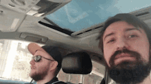 a man with a beard is sitting in the driver 's seat of a car with another man