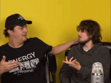 a man wearing a black shirt that says energy is talking to another man