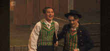 a man and a woman are standing next to each other and the man is wearing a green vest
