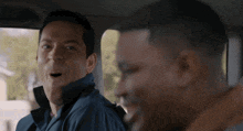 two men are sitting in a car and one is making a funny face