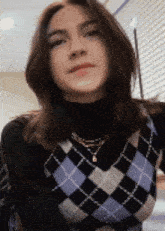 a woman is wearing a black turtleneck and a plaid vest