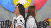two women are sitting back to back with their backs to each other in front of microphones .