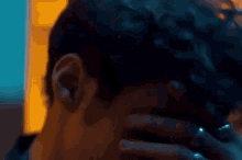 a close up of a man covering his face with his hand while wearing rings .