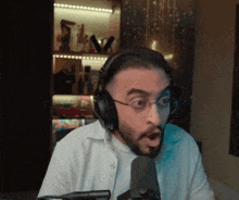 a man with a beard is wearing headphones and glasses and talking into a microphone .