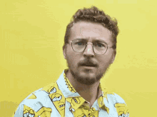 a man wearing glasses and a yellow shirt with simpson faces on the collar