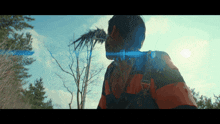 a man in an orange and black striped shirt is standing in the woods