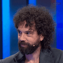 a man with curly hair and a beard is wearing a suit